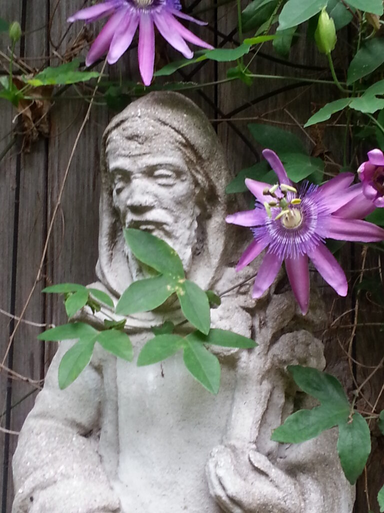 Stone statue with purple flowers and leaves.